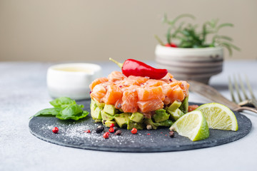 Delicious avocado and raw salmon salad, tartare, served on a black plate with lime, light background