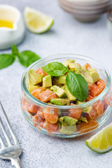 Delicious avocado and raw salmon salad, tartare, served glass jar with lime, light background