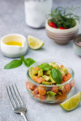 Delicious avocado and raw salmon salad, tartare, served glass jar with lime, light background