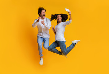 Joyful interracial couple taking selfie while jumping, having fun together