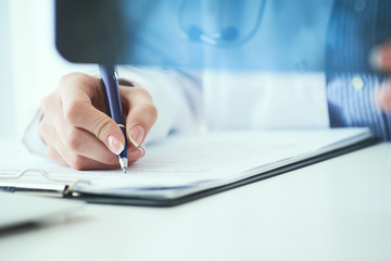 Close up of female doctor holding x-ray or roentgen image and making notes in medical form.