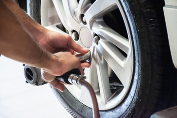 Professional car mechanic using an electric screwdriver to loosen the bolts for changing car wheel...