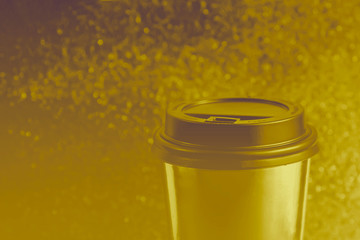 Metallic glass of paper for coffee or tea, standing on the table against of gold background . Color of the year concept. Space for text.