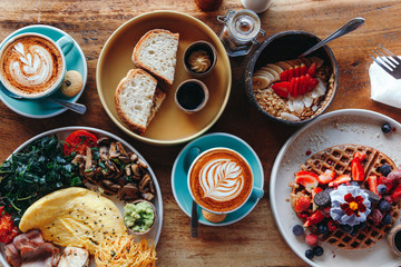 Morning breakfast on a table above, waffles with cream, berries, coffee, cappuccino, bowl, omlet with vegetables, bread with butter, avocado cream, vegan food, healthy food, meal. - obrazy, fototapety, plakaty