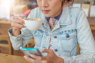 A girl sitting in a coffee shop at a wooden table drinking coffee and using a smartphone on the table as a laptop Girl surfing the internet chat blog With friends on the phone and watch on his screen