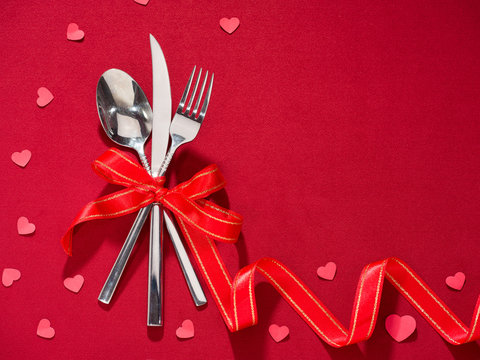Fork and knife in spoon tied with red ribbon on red cover. ackgrounds for special days ( Valentine's Day, Wedding anniversary, birthday. dating, Christmas, New Year and Mother's Day )