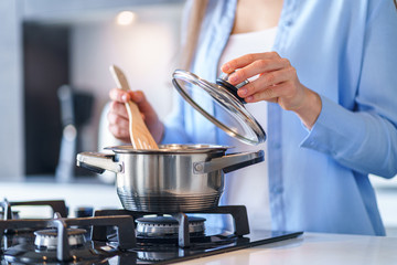 Woman housewife using steel metallic saucepan for preparing dinner in the kitchen at home. Kitchenware for cooking - obrazy, fototapety, plakaty