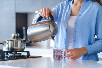 Woman using silver metal electric kettle for boiling water and making tea at home. Household kitchen appliances for makes hot drinks
