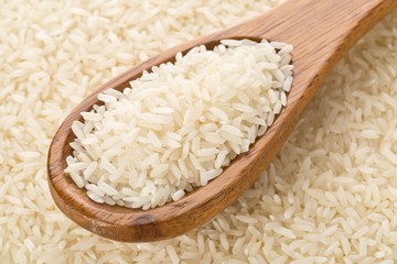 Heap of white uncooked, raw long grain rice in wooden spoon on rice kernels background