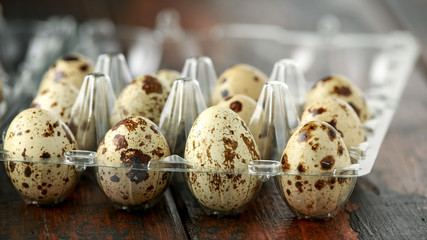 Quail eggs in transparent plastic container on wooden table