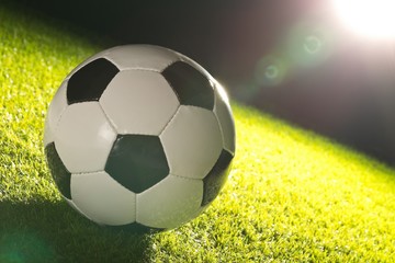 Single soccer ball on green grass lawn background with lensflare from stadium light