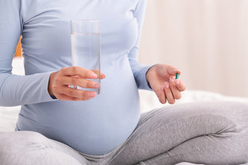 Unrecognizable Pregnant Lady Holding Pill And Water Sitting On Bed
