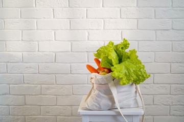 Craft cotton bag with natural products, sunlight on white brick wall background. Healthy food, diet, nutrition concept. Close-up, copy space