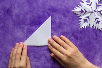 Woman hands holding made folded paper triangle on the violet surface