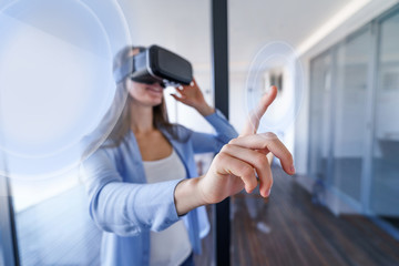 Obraz premium Amazed surprised young woman with virtual reality glasses touching the air during the VR experience at home