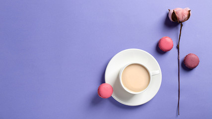 white cup of coffee with milk and tasty macarons, cotton flower on a delicate lilac background. top view, copy space. spring greeting card, wallpaper, banner