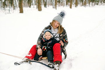 Fototapeta na wymiar Mother and child having fun sledding in winter park. Happy family enjoying on winter holiday