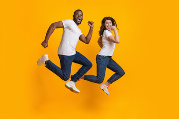 Fototapeta na wymiar Funny interracial couple jumping and running in the air, yellow background