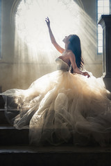 silhouette portrait of bride in white dress sitting on stairs infrontof window with sunlight pass through