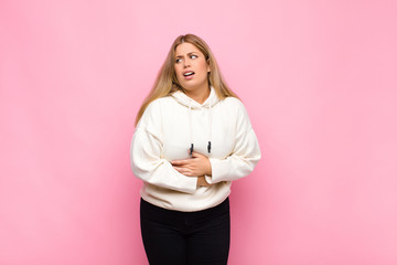 young blonde woman feeling anxious, ill, sick and unhappy, suffering a painful stomach ache or flu...
