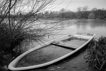 a sunken rowing boat lies on the shore of a frozen small lake