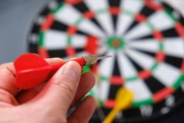 Read in the hands of a man taking aim with green darts, dart board and darts,