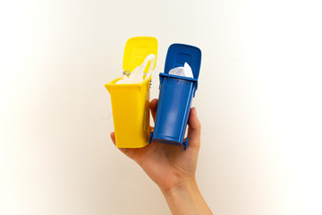 Hand holds two small garbage cans, yellow and blue. Sort garbage in different trash bins for recycling
