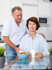 Obraz na płótnie Canvas Happy mature couple posing near kitchen table and drinking tea