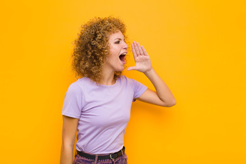 young afro woman yelling loudly and angrily to copy space on the side, with hand next to mouth...