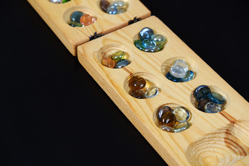 wooden mangala game, mangala game board and glass marbles, on black background