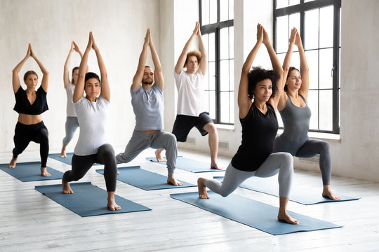 Young diverse people doing Warrior one exercise, practicing yoga