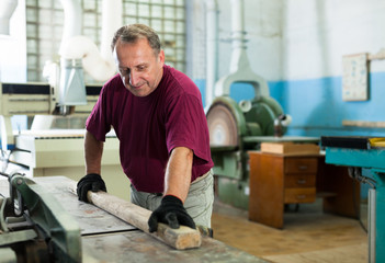 Concentrated worker is shaping timber on woodworking machine at the factory