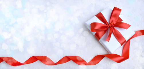 Valentines day composition of gift box with red ribbon on white background. Greeting concept for Mothers day, Women day or wedding. Bokeh lights. Banner with copyspace.
