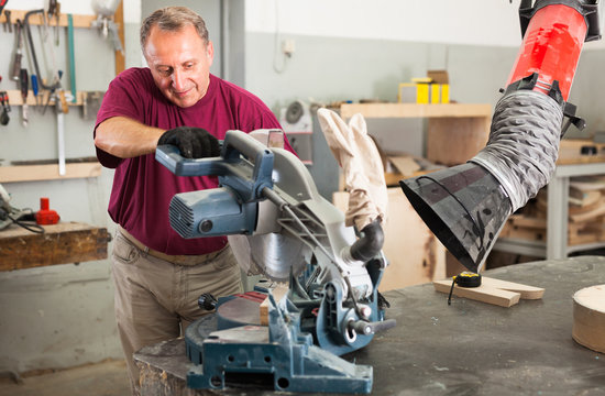 Confident workman cutting wooden planks using circular saw