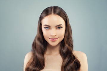 Beautiful healthy woman with long brown hair smiling on blue background. Facial treatment, moisturizing and skin care concept