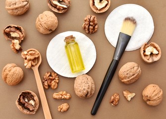 Walnut oil in small bottle, cosmetic brush, natural skin and hair care product, flat lay on brown background. 