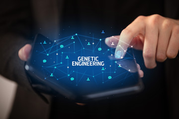 Businessman holding a foldable smartphone with GENETIC ENGINEERING inscription, new technology concept