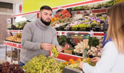 Female seller assisting customer to weigh grape