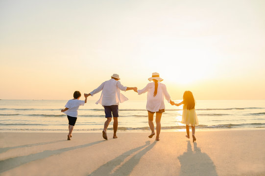 Family, travel, beach, relax, lifestyle, holiday concept. Family who enjoy a picnic. Parents are holding hands their children and walking on the beach at sunset in holiday.