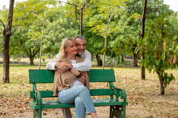 Happy Senior Caucasian couple hugging together at the bench in park