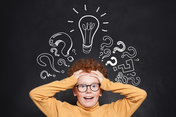 Portrait of funny child boy with lightbulb on blackboard