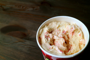 Creamy strawberry cheesecake ice cream in a big cup on dark brown wooden table