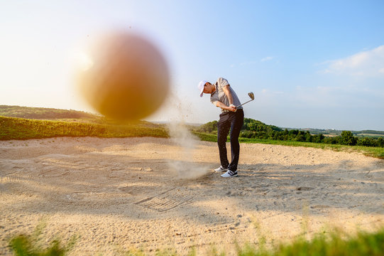 lifestyle, golf, activity, outdoor, sport, golfer concept. A close-up golf ball blurred by man is sweeping golf on the sand at a golf course in the summer. Sport lifestyle Concept. Bright picture.