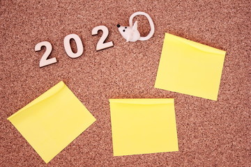 The white mouse and number 2020 and writing paper are laid out on a wooden surface. New Year planning.