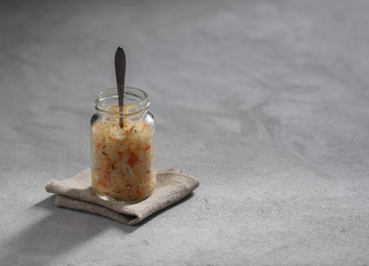 Sauerkraut with carrots and cumin in a jar on a linen napkin with a wooden spoon in a rustic style on a dark background