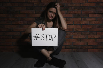 Crying young woman with hashtag STOP near brick wall. Domestic violence concept