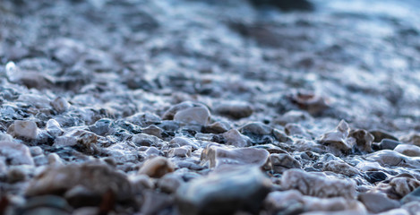 Gravel pebbles at the beach shore, cold photo. Wet stones reflecting sunlight , many different...