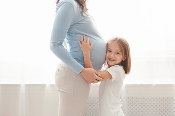 Little cute girl embracing her pregnant mother belly