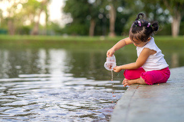 Cute little girl sitting along the lake feeding carp fishes.