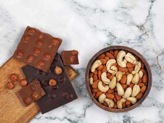 Broken chocolate bars, raw hazelnuts, almonds and cashew on gray marble background